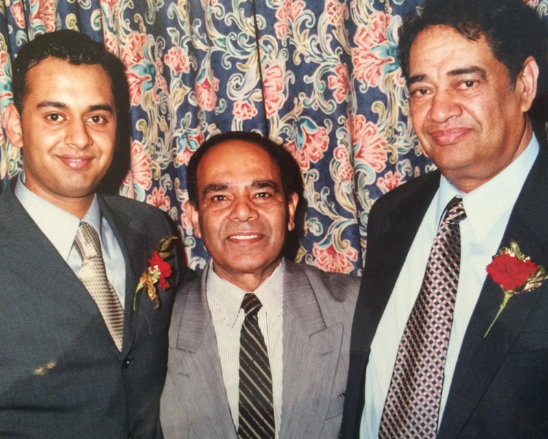 Three men in suits with red boutonnieres posing in front of floral backdrop