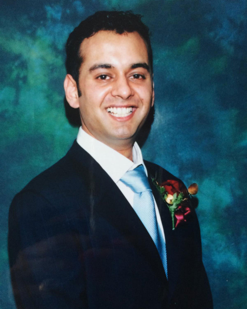 Man in formal suit with blue tie and red boutonniere against green-blue backdrop